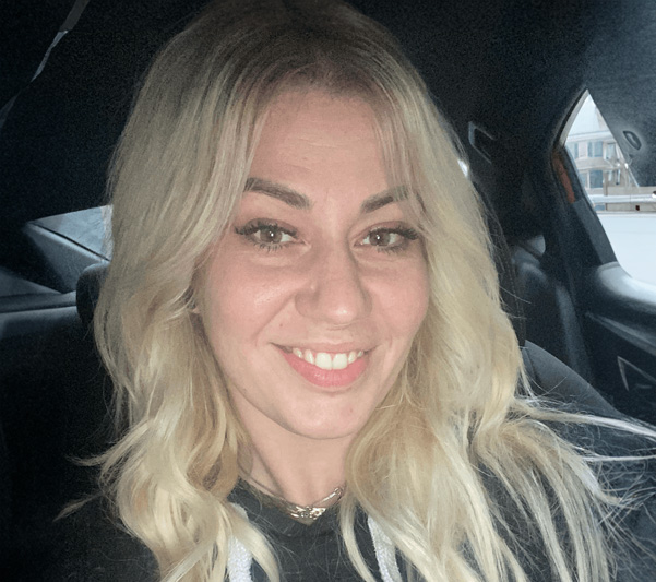 The image features a woman with blonde hair, smiling at the camera, sitting inside a car.