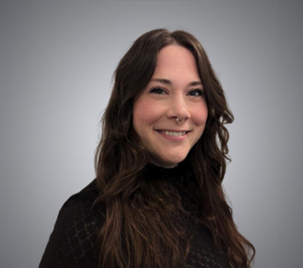 A smiling woman with long hair, wearing a dark top, stands against a neutral background.