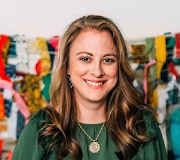 A woman with a smiling expression posing in front of colorful fabric items.
