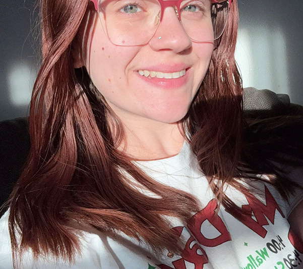 A person with red hair and glasses smiling at the camera.