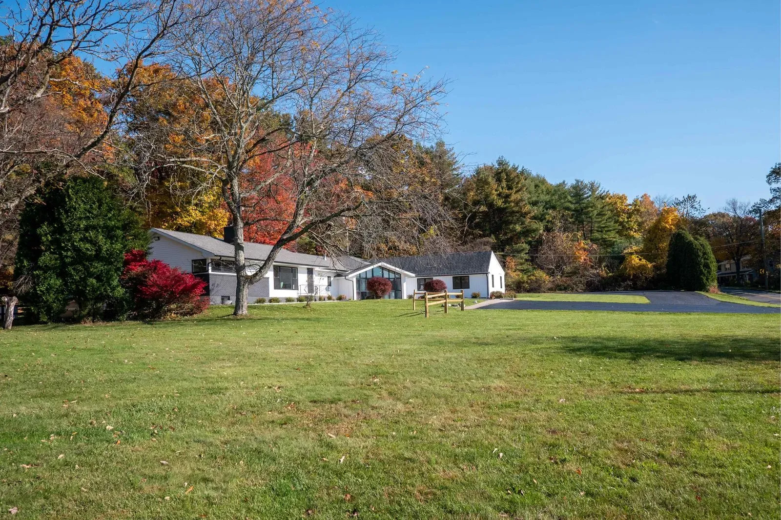 The image depicts a serene suburban scene with a two-story house, a driveway, a yard, and autumn foliage on trees.