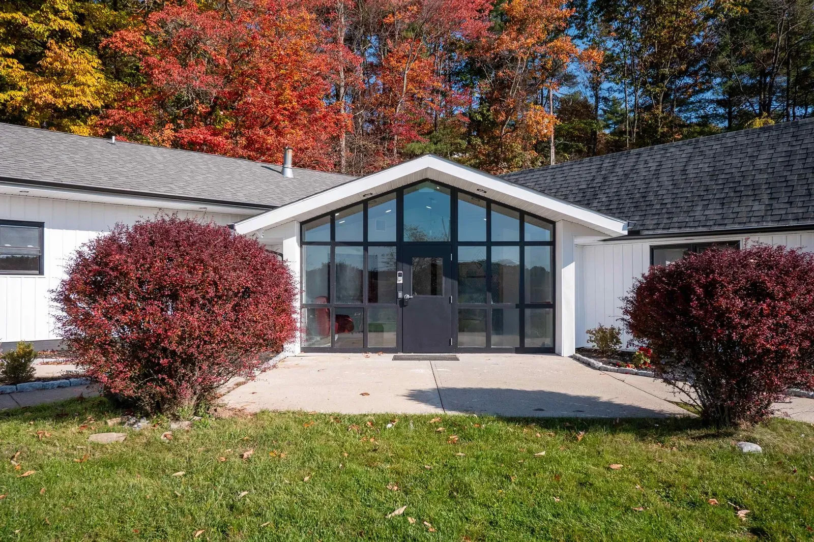 The image depicts a modern building with a prominent glass facade, situated in an outdoor setting with autumn foliage and a clear sky.