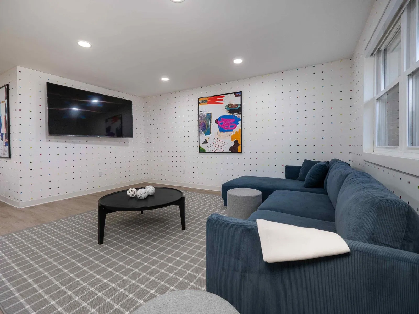 The image shows an interior room with a modern design featuring a patterned wall, a gray carpet, dark furniture, and white walls with decorative elements.